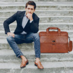 Professional man carrying the tan leather briefcases for men by the top handle. Export to Sheets